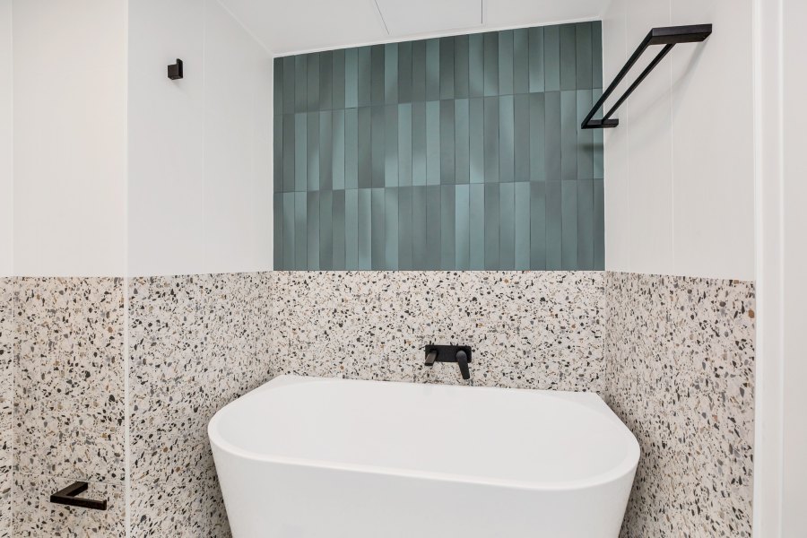 Bathtub with green accent wall and terrazzo tiles